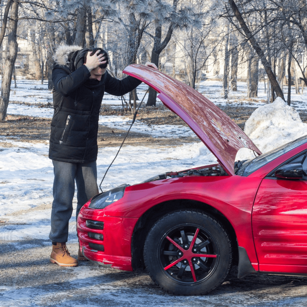 Person looking under the hood of a car on a snowy day